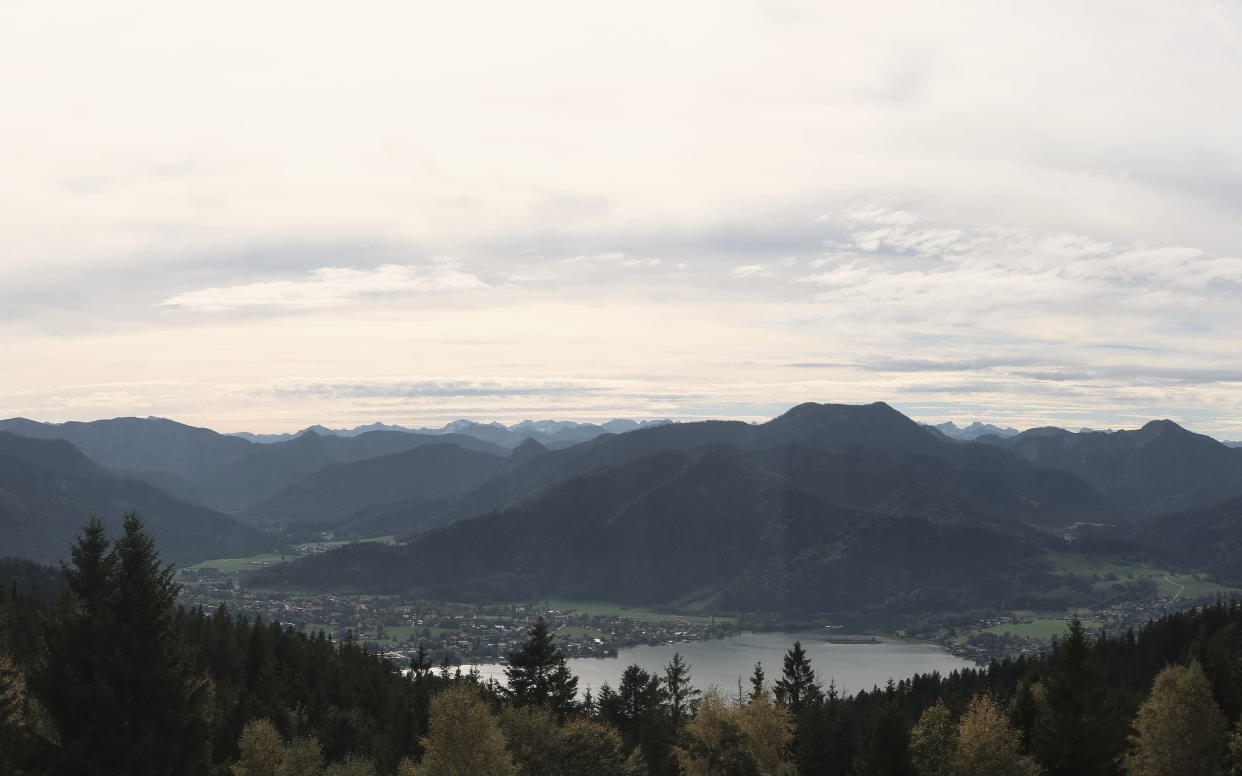 Herbstlicher Blick über Wald und See auf die Berge des Tegernseer Tals